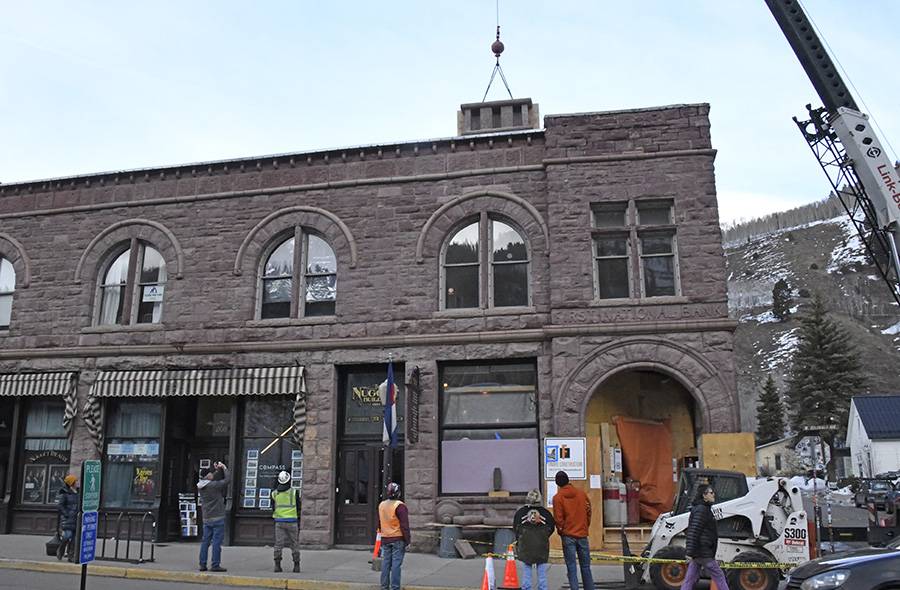 The historic First National Bank building in Telluride during its restoration, with its new tower being lifted into place by crane.